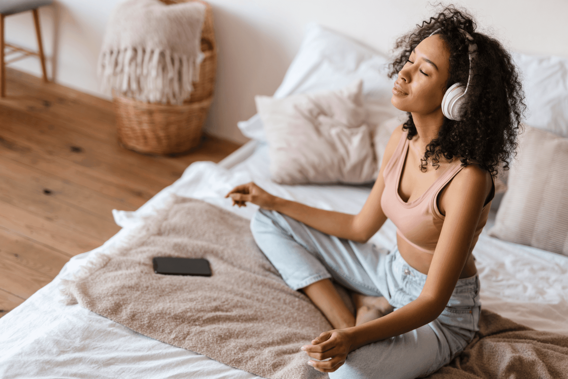 Lady peacefully meditating on her bed with headphones on